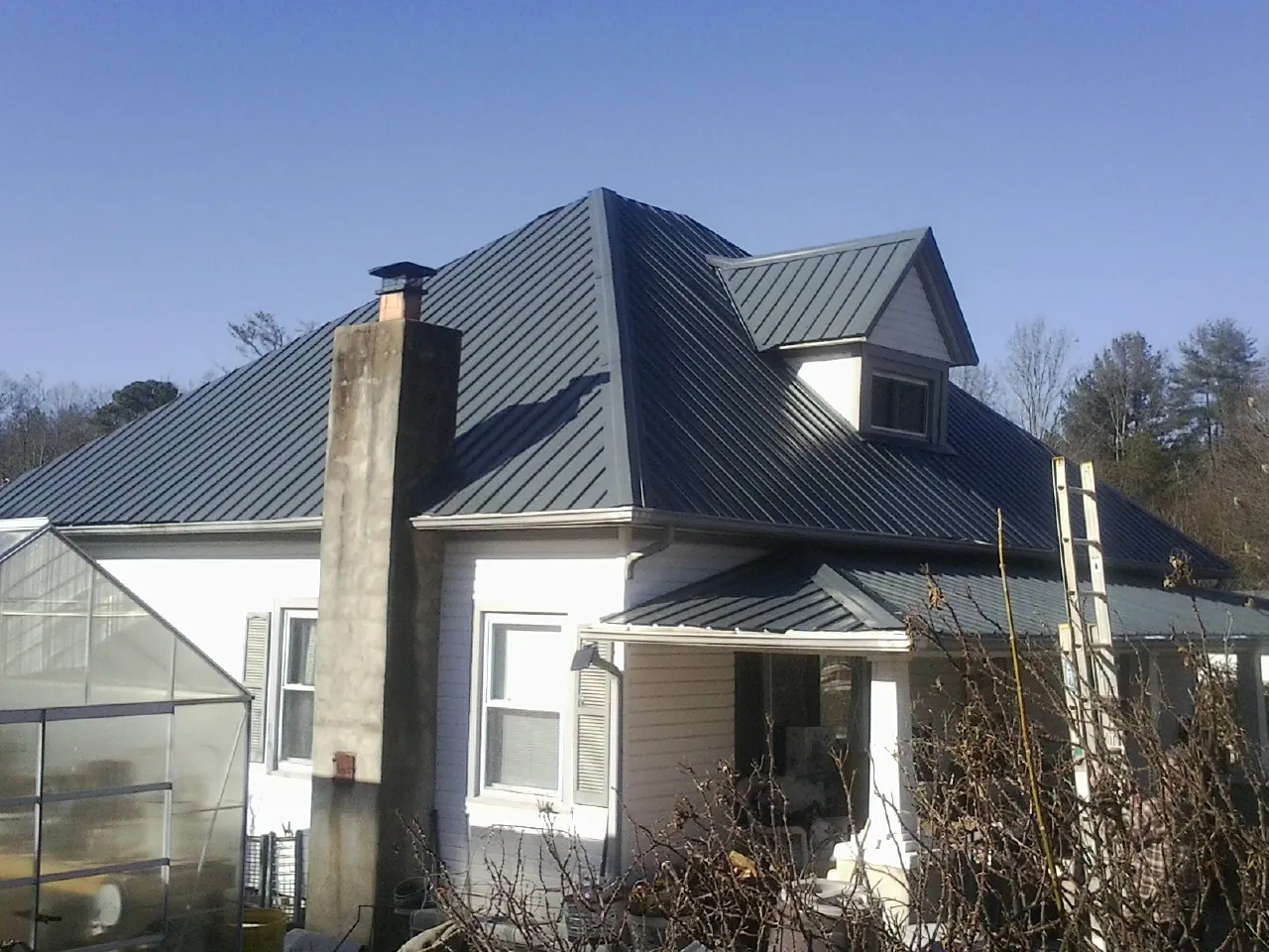 Dark blue standing seam metal roof on a white farmhouse with dormer — Slate & Tile Roof Repair by Roofing Brothers in Walcott