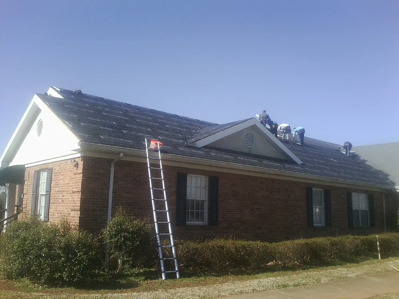 Crew tearing shingles off a brick ranch roof with a ladder set — Emergency Roof Repair work by our crew in Walcott