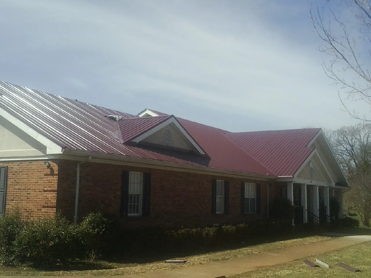 Red metal roof with gabled entries on a long brick building, from a Hail Damage Roof Repair job in Walcott