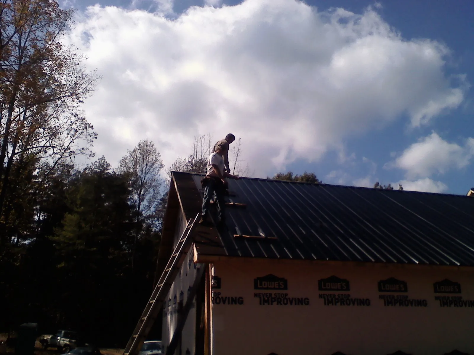 Roofer fastening dark metal panels high against a cloudy sky, from a Roof Inspection job in Walcott